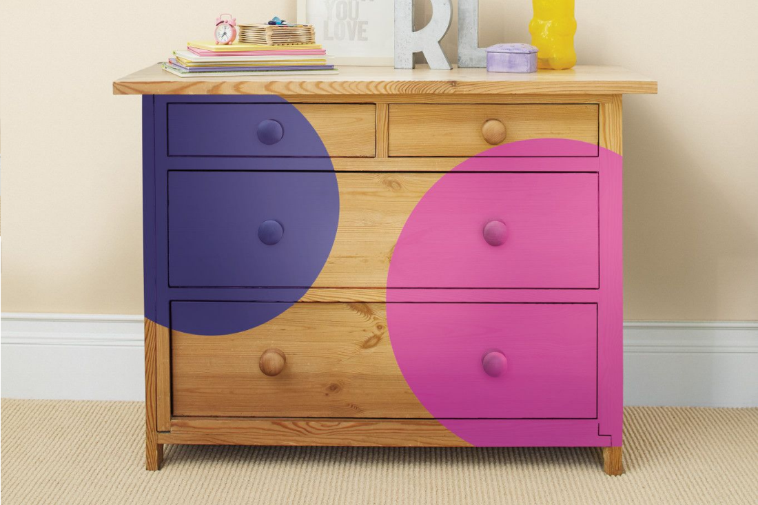 A warm wood bedroom dresser is painted with two large dots of color – one is purple and one is pink.