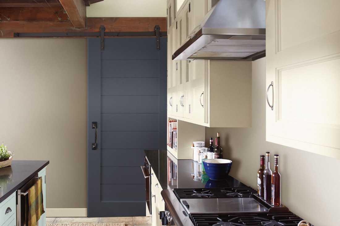 Modern galley kitchen with a deep blue painted barn door at the end and bright cabinets, paired with dark countertops.