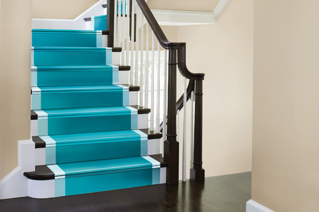 A traditional staircase winds down from above, the stairs and treads are painted a deep aqua, framed by a light blue.