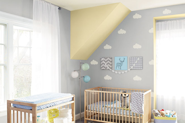 A nursery features stenciled on white clouds on a grey wall providing a whimsical feel. Ceiling is painted yellow.