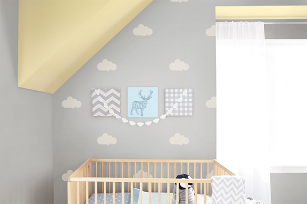 A nursery features stenciled white clouds on a grey wall providing a whimsical feel. Ceiling is painted yellow.