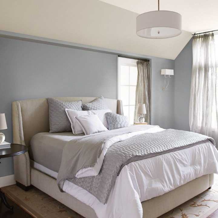 Gray-toned, sunny bedroom with a king size bed and pendant ceiling light. Walls painted ironed gray.