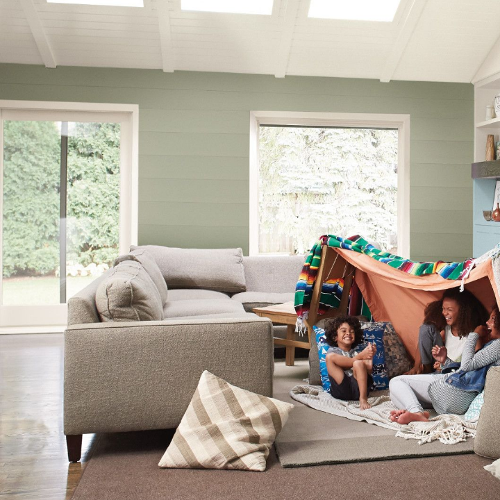 Kids sit under a living room fort made of blankets, laughing, with couches, rugs and Graywood painted walls.