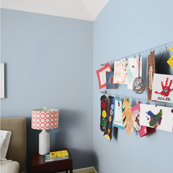 Bedroom with a kids’ artwork hanging from string on a tempest wind painted wall.