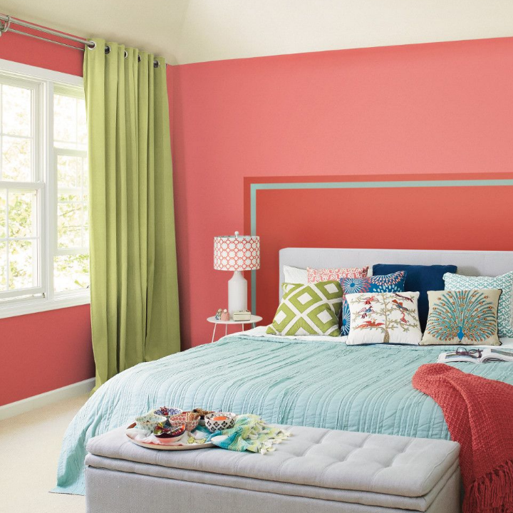 A sunny bedroom with subtle blue and green blankets and pillows. Walls painted carmela coral.
