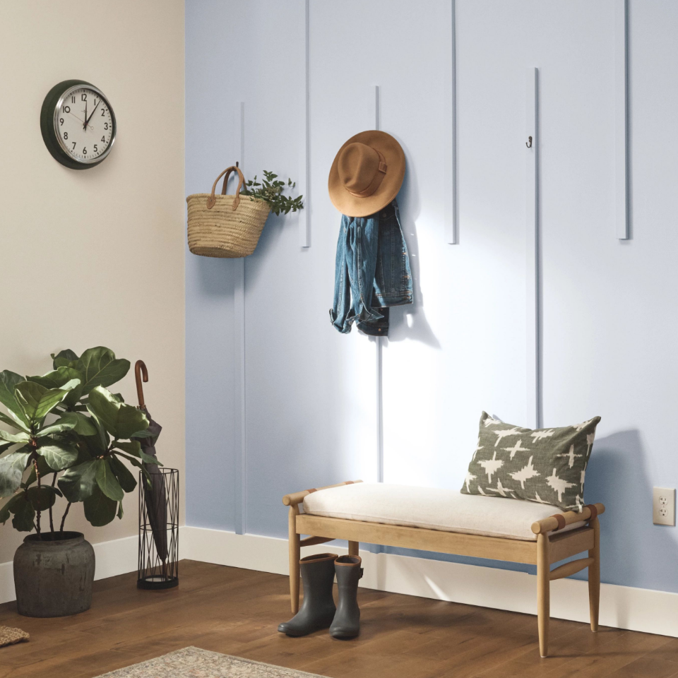 Mudroom with hooks on whispered-colored walls, hanging a jacket and hat. Sitting bench with throw, boots on ground.