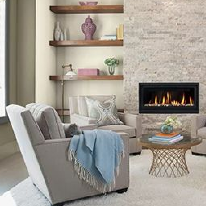 Cozy living room with accent chairs, a fire in the fireplace and well-curated bookshelves. Wall color is weathered rock gray.