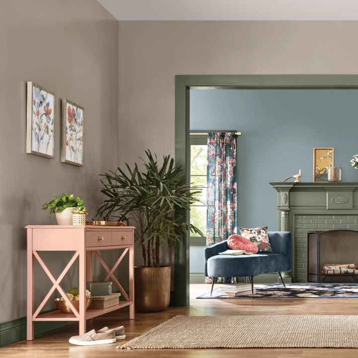 Living room painted neutral rustic greige, with green trim. Floor plants, pink console table and rug make it cozy.