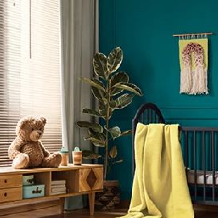 Nursery with a crib and yellow blanket, a console table with a teddy bear, and walls painted the color sea depths blue.