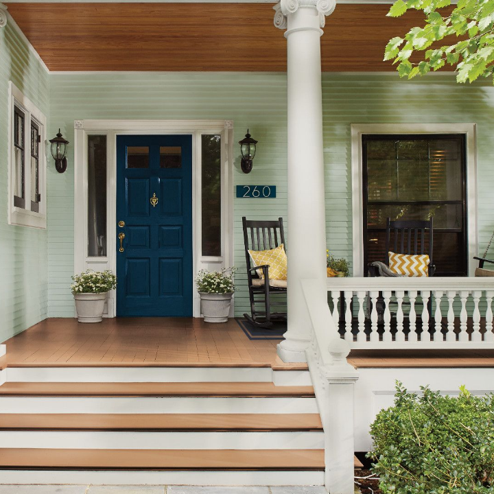 Front porch of a home with rocking chairs. A blue front door and teal siding give way to the porch, painted sweetened tea.