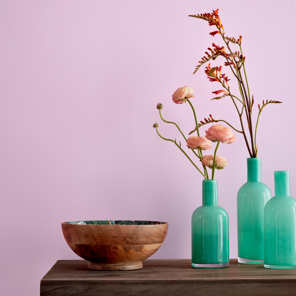 A wood console table with teal vases containing flowers and a wooden bowl sits against a wall painted sleepy purple.