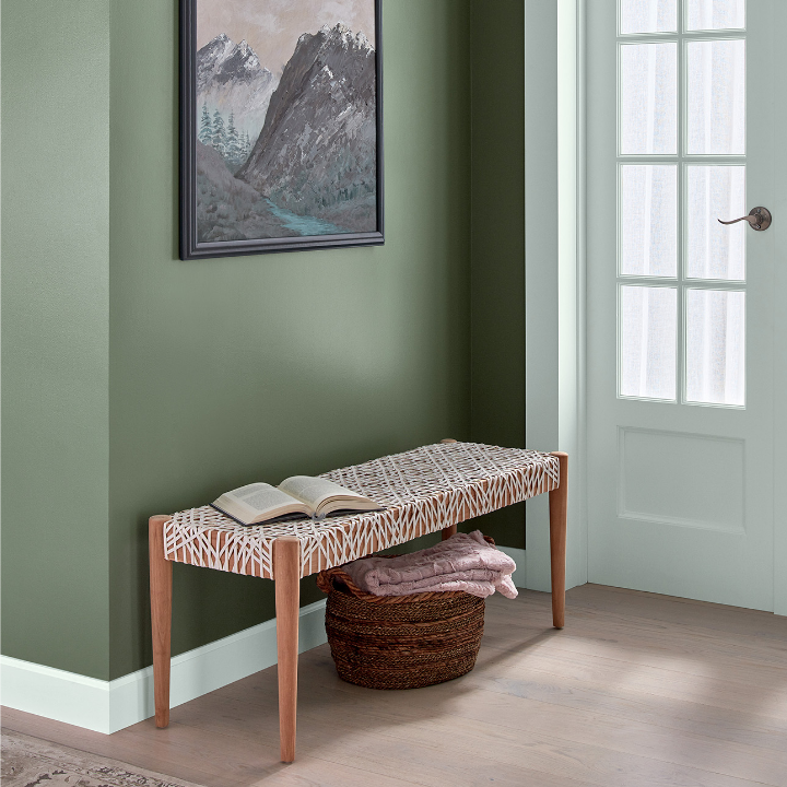 Entryway with modern bench seat and basket that holds blankets. Framed art hangs on the wild basil colored wall.