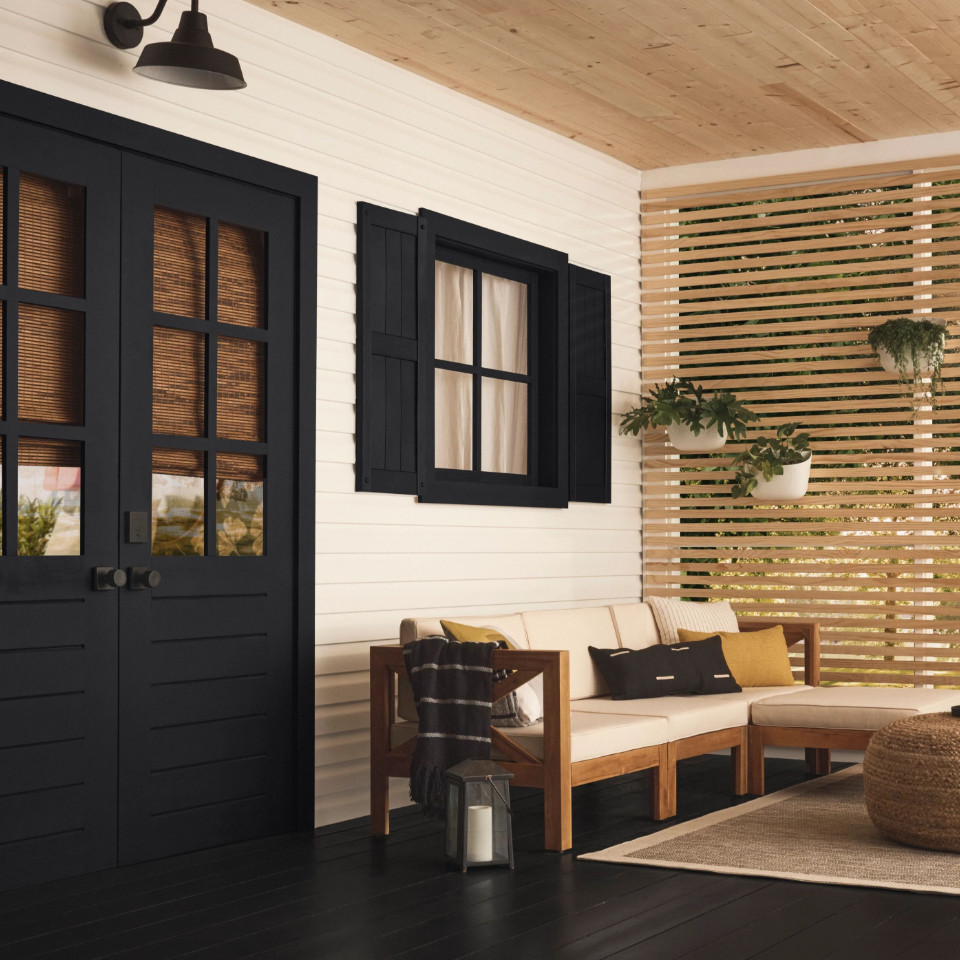 Beautiful enclosed porch living area, white siding, black trim and black floor with elegant, Japandi-style furniture.