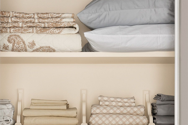 Linen closet with built-in wood shelving painted the color dust flats, bedroom linens sit atop the shelves.