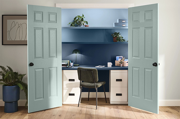 A home office situated inside of a closet with French doors painted light teal. Wall and shelves in office are darker blue. 