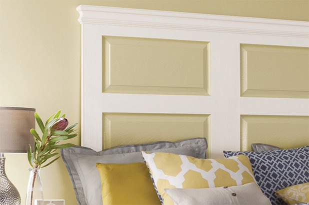 A bed with patterned pillows and blankets sits in front of a wall painted with a yellow and white paneled headboard.