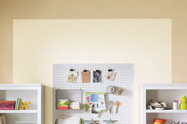 A smaller crafting room with shelving and pegboard. A dual-toned wall is light beige framed by darker beige.  
