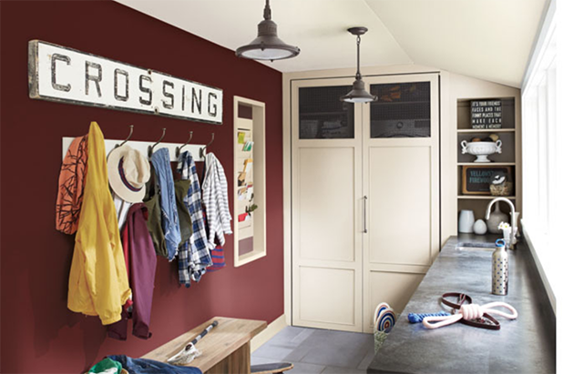 Mudroom with coats, hats and shirts hanging on hooks, a vintage railroad sign sits on walls painted gayles rouge.