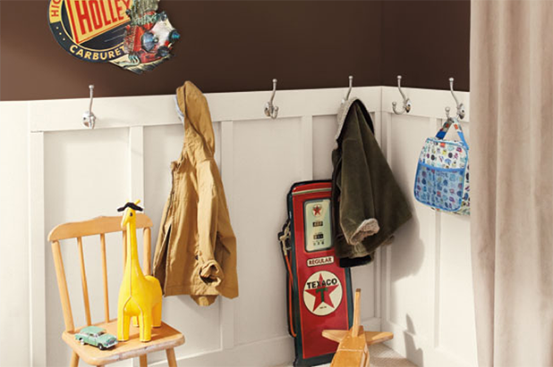 Mudroom with coats hanging on hooks and retro gas station signage with a brown colored wall and white wainscotting. 
