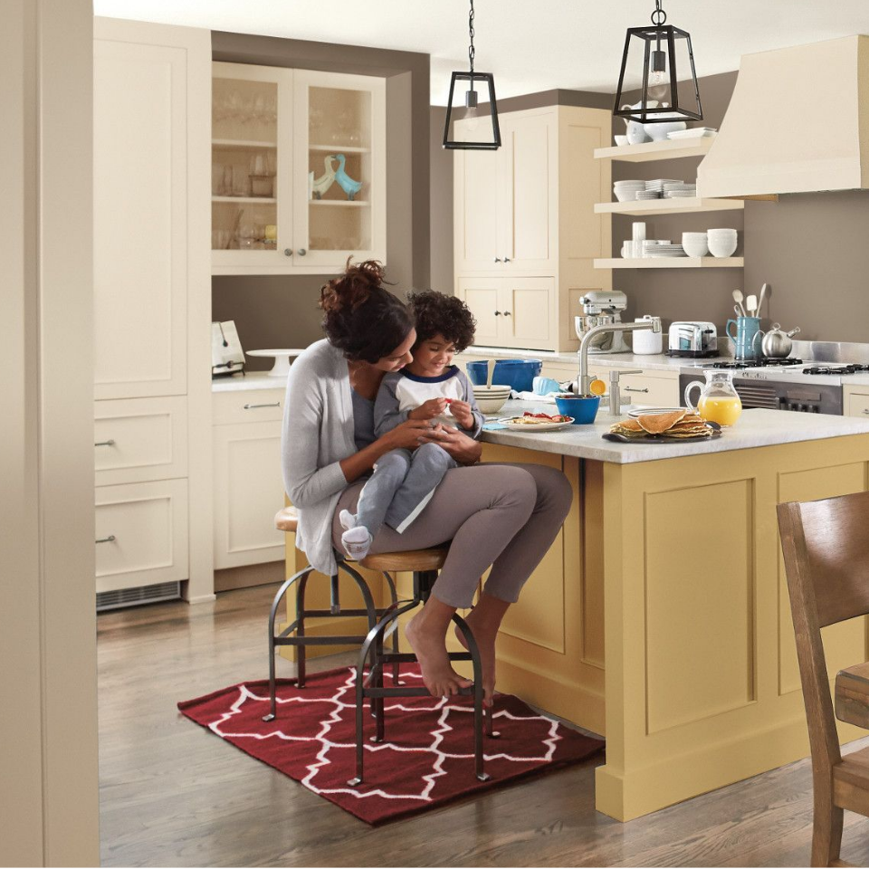 Child sits in his mom’s lap, on a stool at a kitchen counter with breakfast served. Cabinets painted white rapids.