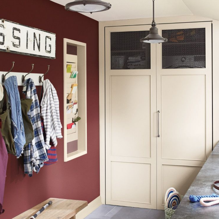 Mudroom with coats, hats and shirts hanging on hooks, a vintage railroad sign sits on walls painted gayles rouge.