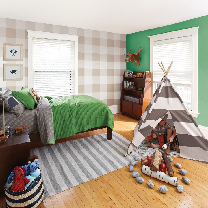 Child plays in a toy tent in a bedroom. Plush toys rest in a basket and side table. Walls painted botanic 