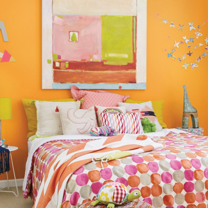 Bright colored bedroom with multi-colored sheets and pillows. Wall color is marigold glow.