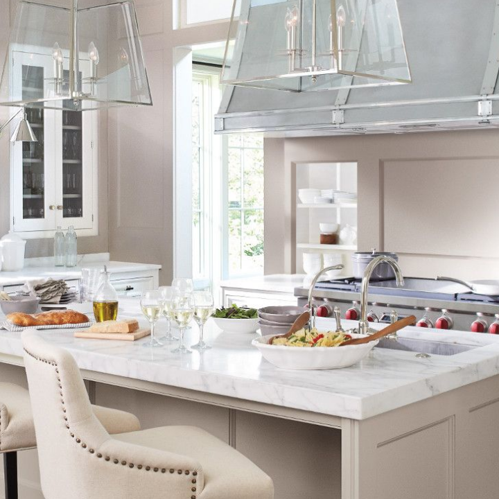 Large marble-topped kitchen island with massive range and hood in background. Walls painted the color sultry gray.