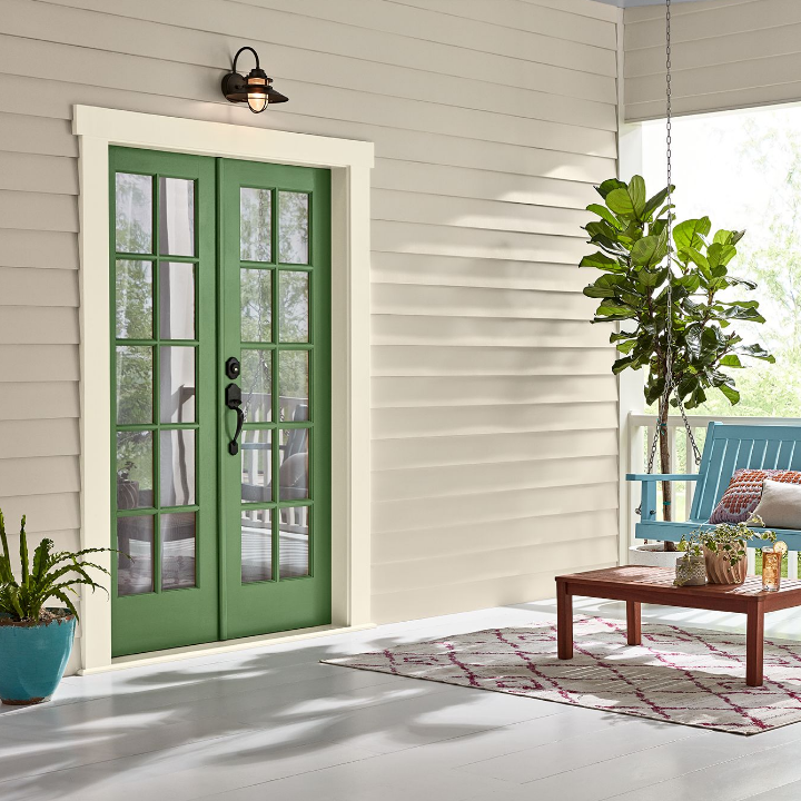 Sun-drenched, warmed silver deck with outdoor rug, coffee table and potted plants, with green-colored French doors. 