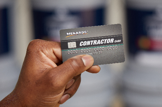 Hand holding up Menards Contractor Card with stack of Dutch Boy Professional Series products in background.
